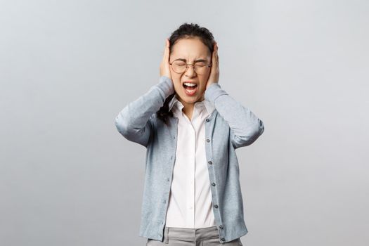 People, emotions and lifestyle concept. Stop it, cant bear listen to you anymore. Depressed young fed-up asian woman scream from discomfort and annoyance, shut ears not hear noisy annoying sound