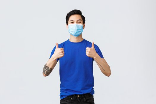Different emotions, social distancing, self-quarantine on covid-19 and lifestyle concept. Cheerful and supportive young asian guy in medical mask encourage use personal protective equipment