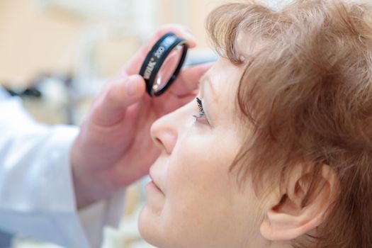 A male ophthalmologist checks the eyesight of an adult woman with a binocular ophthalmoscope