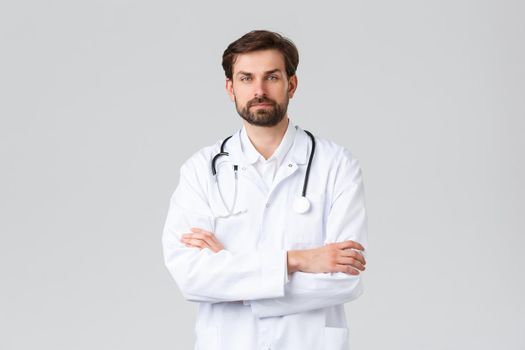 Hospital, healthcare workers, covid-19 treatment concept. Professional doctor in white scrubs with stethoscope, cross arms chest confident, looking camera, treating patients, grey background