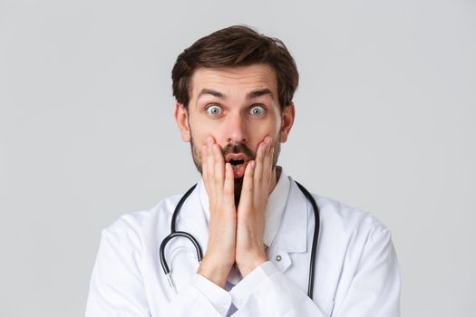 Hospital, healthcare workers, covid-19 treatment concept. Close-up shot of amazed, speechless doctor, gasping open mouth and staring astonished, hold hands near mouth impressed over big news