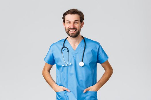 Covid-19, quarantine, hospitals and healthcare workers concept. Cheerful smiling doctor or nurse with stethoscope and scrubs, friendly talking to coworker or patient, grey background