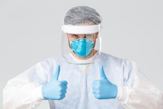 Covid-19, pandemic, healthcare workers fighting virus outbreak. Confident professional medical stuff, doctor in hospital show thumb-up, wear protective suit, safe people lives in clinic, wait vaccine