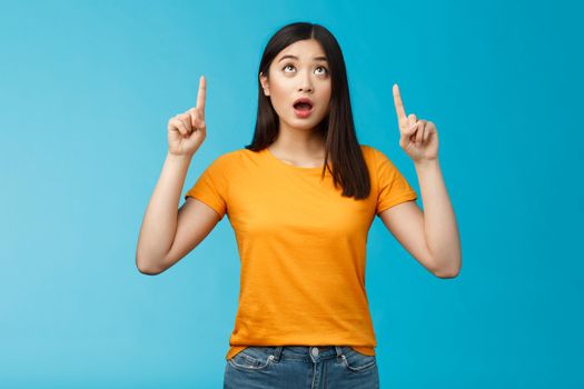 Surprised impressed asian girl dark short hairstyle drop jaw, gasping amazed look pointing up astonished, check out incredible offer, express full disbelief and amazement, stand blue background