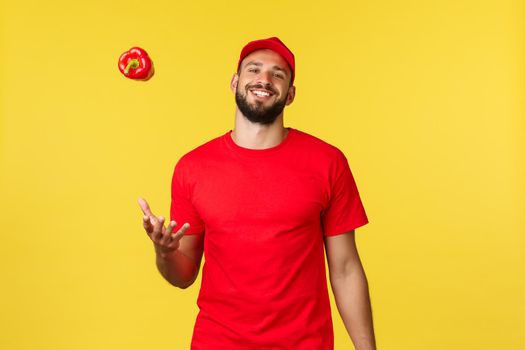Online delivery, shopping and food order concept. Carefree smiling courier in red uniform cap and t-shirt, throwing red pepper and look friendly, express deliver order from grocery shop