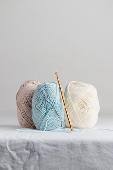 Crochet hook and balls of cotton yarn pastel colors on a white table