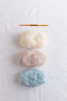 Crochet hook and balls of cotton yarn pastel colors on a white table
