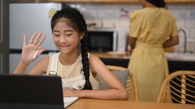 Smiling Asian girl having online class on computer tablet at home. Concept of Virtual education, homeschooling