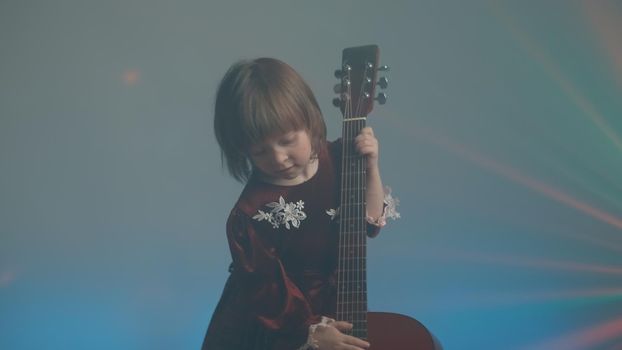 Little girl in a vintage dress plays an acoustic guitar like a double bass