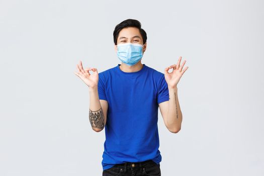 Different emotions, social distancing, self-quarantine on covid-19 and lifestyle concept. Glad happy asian man in medical mask, show okay sign, approve and like idea, recommend product