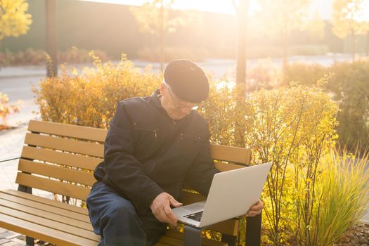 Elderly man use laptop in the park. Handsome senior man in glasses work outside.