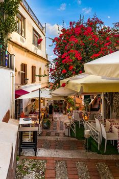Beautiful old town of Taormina with small streets, flowers. Architecture with archs and old pavement in Taormina. Colorful narrow street in old town of Taormina. Sicily, Italy. 