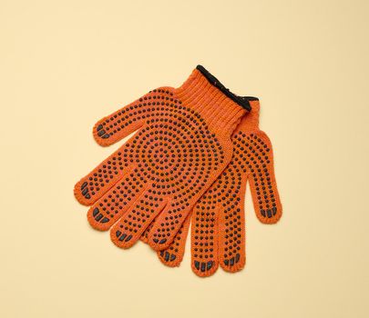 Textile orange work gloves on a yellow background.