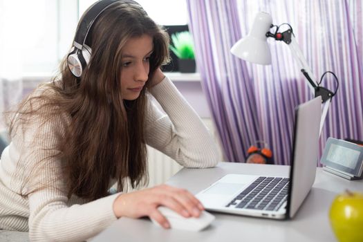 A young brunette is homeschooling remotely via the internet and laptop.