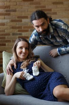 A man and his pregnant wife pose on a sofa in their home.