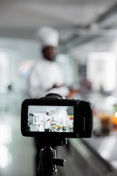 Close up of camera recording head cook preparing gourmet dish for culinary school in restaurant kitchen.