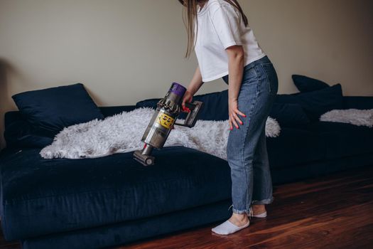 Woman cleaning sofa with a modern cordless vacuum cleaner with a special nozzle, close-up. Dry cleaning concept with wireless vacuum cleaner.