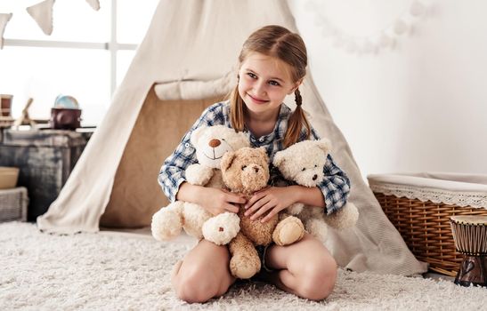 Little girl hugging plush teddies and smiling