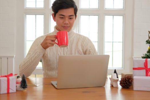 man holding coffee cup & using computer at home during christmas. xmas new year celebration