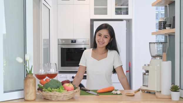 Healthy young woman standing at kitchen counter and preparing ingredients for making vegetarian food