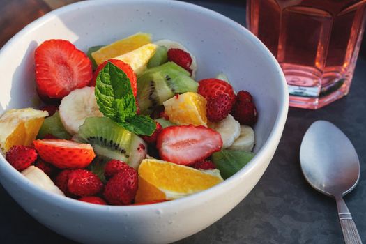 Fruit salad in a white bowl on a tray with a drink and a spoon