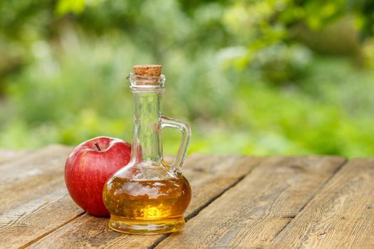 Apple vinegar in glass bottle and fresh red apple on wooden boards