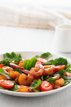 Fresh salad of shrimps, tomatoes, arugula and herbs on a white plate. vertical image