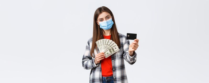 Money transfer, investment, covid-19 pandemic and working from home concept. Girl in medical mask show credit card and cash, prefer using contactless payment method during coronavirus