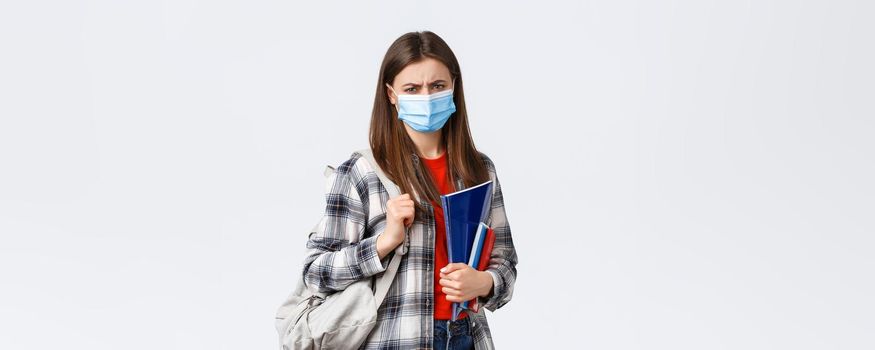 Coronavirus pandemic, covid-19 education, and back to school concept. Upset disappointed female student in medical mask hate studying in university during infection oubreak, frowning condemn dean