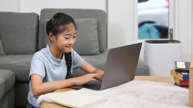 Asian girl having online class, doing homework in living room. Virtual education, homeschooling concept
