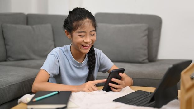 Cheerful Asian girl using smart phone during break from learning online. E-learning, homeschooling concept