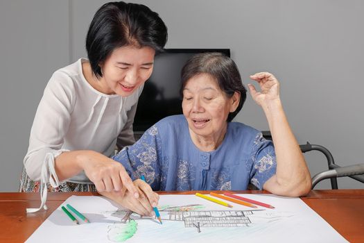 Elderly woman painting color on her drawing with daughter , hobby at home