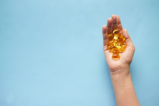 fish oil supplement on hand on blue background