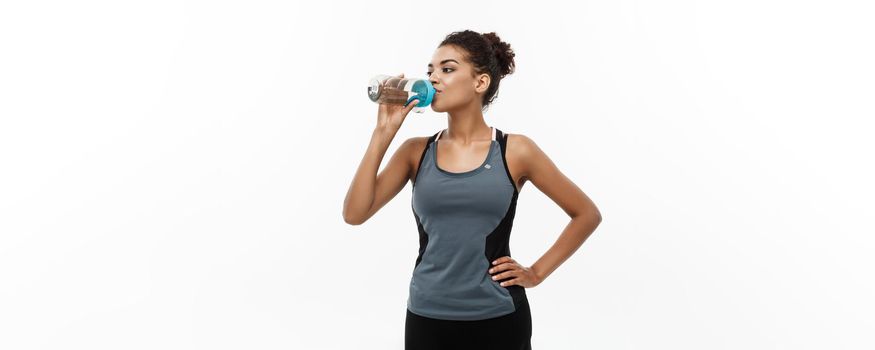 Healthy and Fitness concept - beautiful African American girl in sport clothes drinking water after workout. Isolated on white studio background