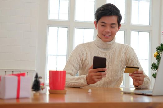 man holding credit card & smart phone for online shopping.  male buyer buying christmas gift on internet. xmas new year holiday celebration