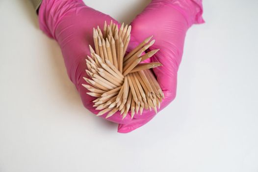 Master in pink gloves holds orange sticks for manicure.