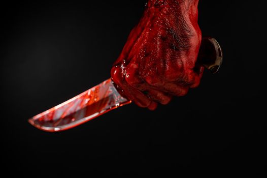 A man with bloody hands brandishes a knife on a black background.