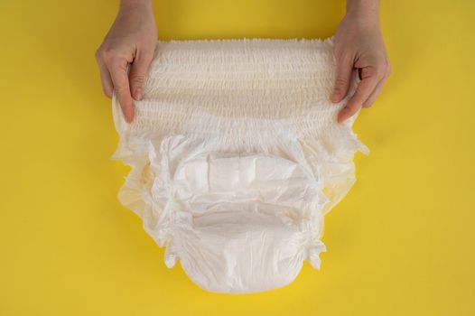 A woman holds an adult diaper on a yellow background. Incontinence problems.