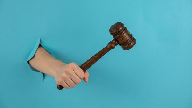 A woman's hand with a wooden judge's gavel sticks out of a hole in a blue background.