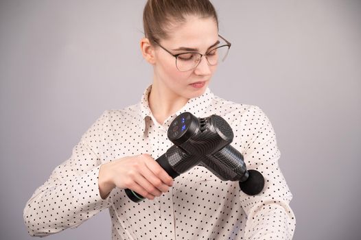 Caucasian business woman massaging her biceps with a percussion massager.