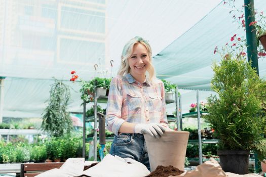 Woman planting a bush in flower pot using dirt in garden center