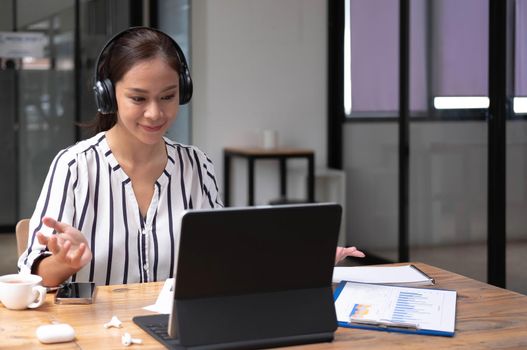 Happy asian young wearing headset, communicating with client via video computer call.