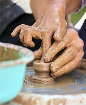 The potter's hands are gently and surely formed by a clay pot on a potter's wheel.