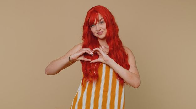 Smiling ginger girl makes heart gesture demonstrates love sign expresses good feelings and sympathy