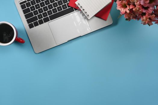 Top view laptop computer, coffee cup, notebook and flower pot on blue background