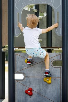 A little boy climbs up a climbing wall on an outdoor playground.