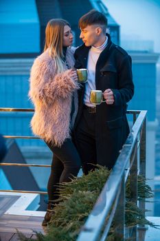 couple with mugs on the terrace of a high-rise building and look at the opening view