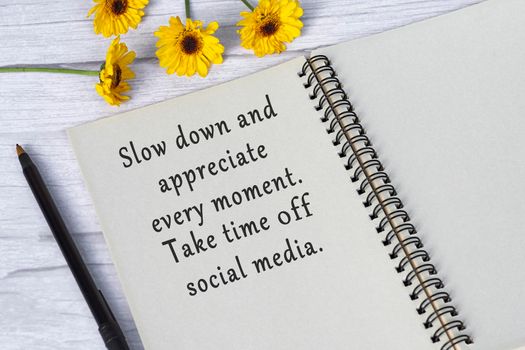 Motivational quote on note book with sunflowers on wooden desk.