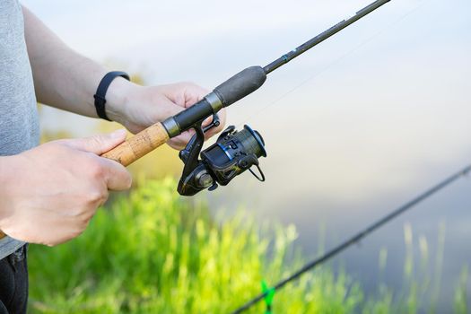 A fishing rod with a spinning reel in the hands of a fisherman. Fishing background. Outdoor recreation.