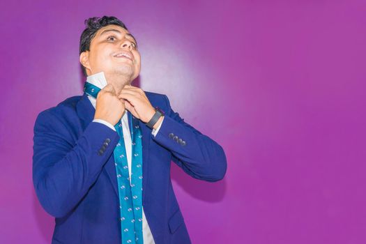 Latin Nicaraguan man in a blue suit having trouble tying his tie knot on a flat background